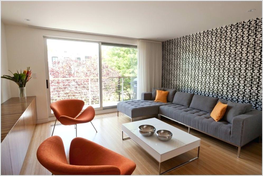 اتاق نشیمن با مبل های طوسی و نارنجی که که یکی از دیوارها دارای کاغذ دیواری سفید و مشکی است و باقی دیوارها به رنگ سفید هستند